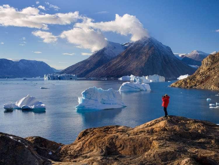 Adventure tourist takes photos of icebergs in Scoresbysund, Greenland, an area visited on an all-inclusive, luxury expedition Seabourn cruise.