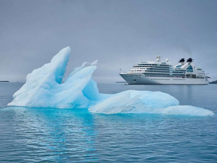 An iceberg floats with a Seabourn ship in background near Arsukfjord, Greenland, an area visited on an all-inclusive, luxury expedition Seabourn cruise.
