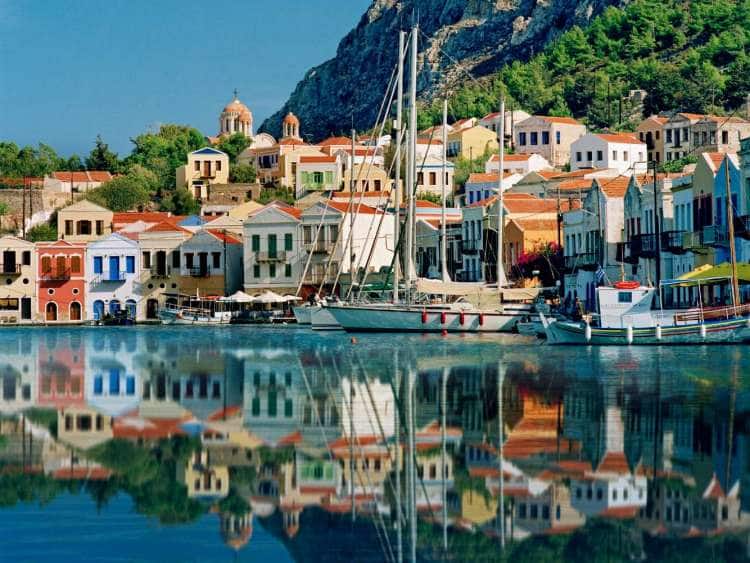 Buildings and boats reflect in the harbor of Kastelorizo, Greece, a port visited on an all-inclusive, luxury Seabourn cruise.