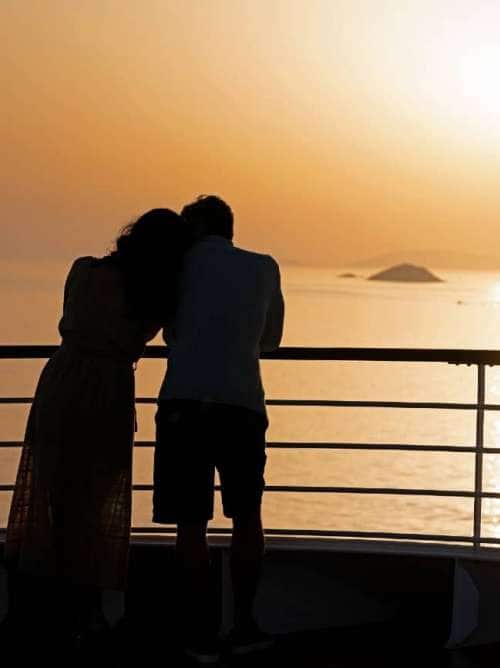 Couple in silhouette enjoying a view of sea islands aboard an all-inclusive, luxury Seabourn cruise.