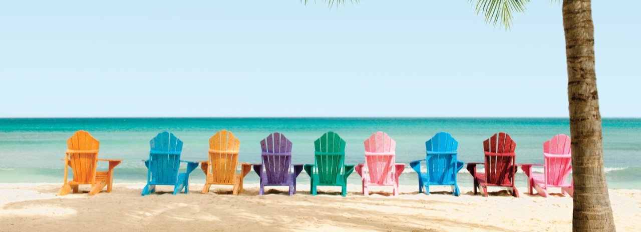Colorful empty, wooden, beach chairs lined up facing the ocean  on a tropical beach