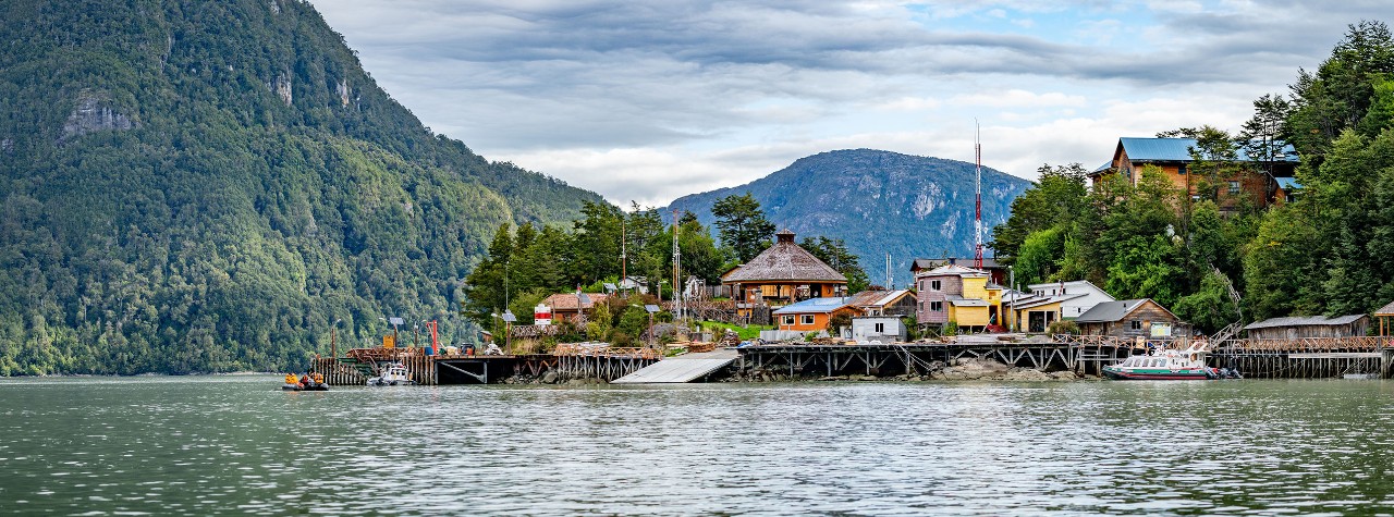Wooden stilt village of Caleta Tortel, Chile, with colorful homes and boardwalks along calm water, backed by steep forested mountains.