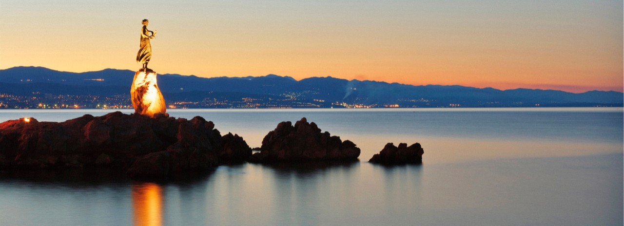 Croatia, Istria, Mediterranean sea, Adriatic Coast, Opatija, The bronze statue girl with seagull, symbol of the city, and the lights of Rijeka in background