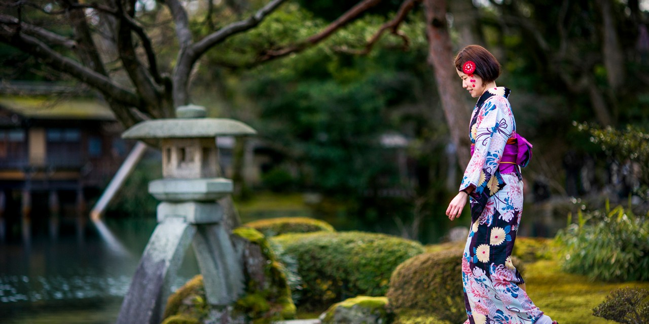 Japan, Chubu, Kanazawa, A girl in traditional dress crosses a bridge in Kenrakuen Gyoen