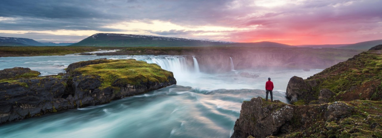 Hiker watching Godafoss waterfall in northern Iceland at sunset.