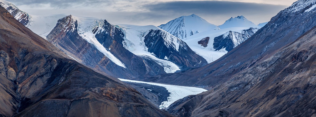 Glacier-filled valley framed by rugged, snowcapped mountains in Northeast Greenland National Park. A hanging glaciers in the mountains of Kaiser Franz Joseph Fjord, Northeast Greenland National Park, at dusk.