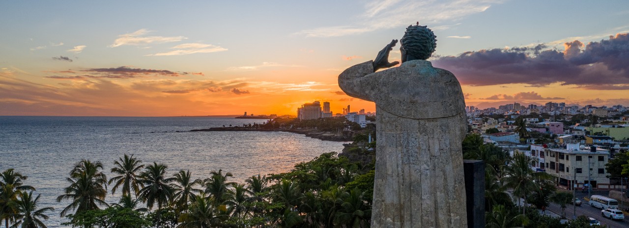 A view looking out to the water at sunset with a large statue in the foreground in Santa Domingo.
