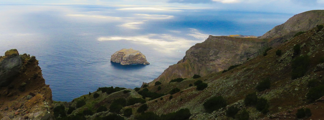 Rugged cliffs overlook the Atlantic Ocean with a rocky islet below on Boatswain Bird Island, St. Helena. Ascension Island, Green Mountain National Park, British Overseas Territory