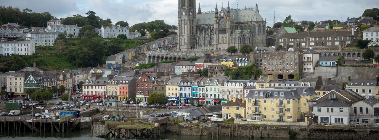 Colorful waterfront town in Ringaskiddy Cork, Ireland, with pastel houses along the harbor and a grand cathedral rising above hillside streets.